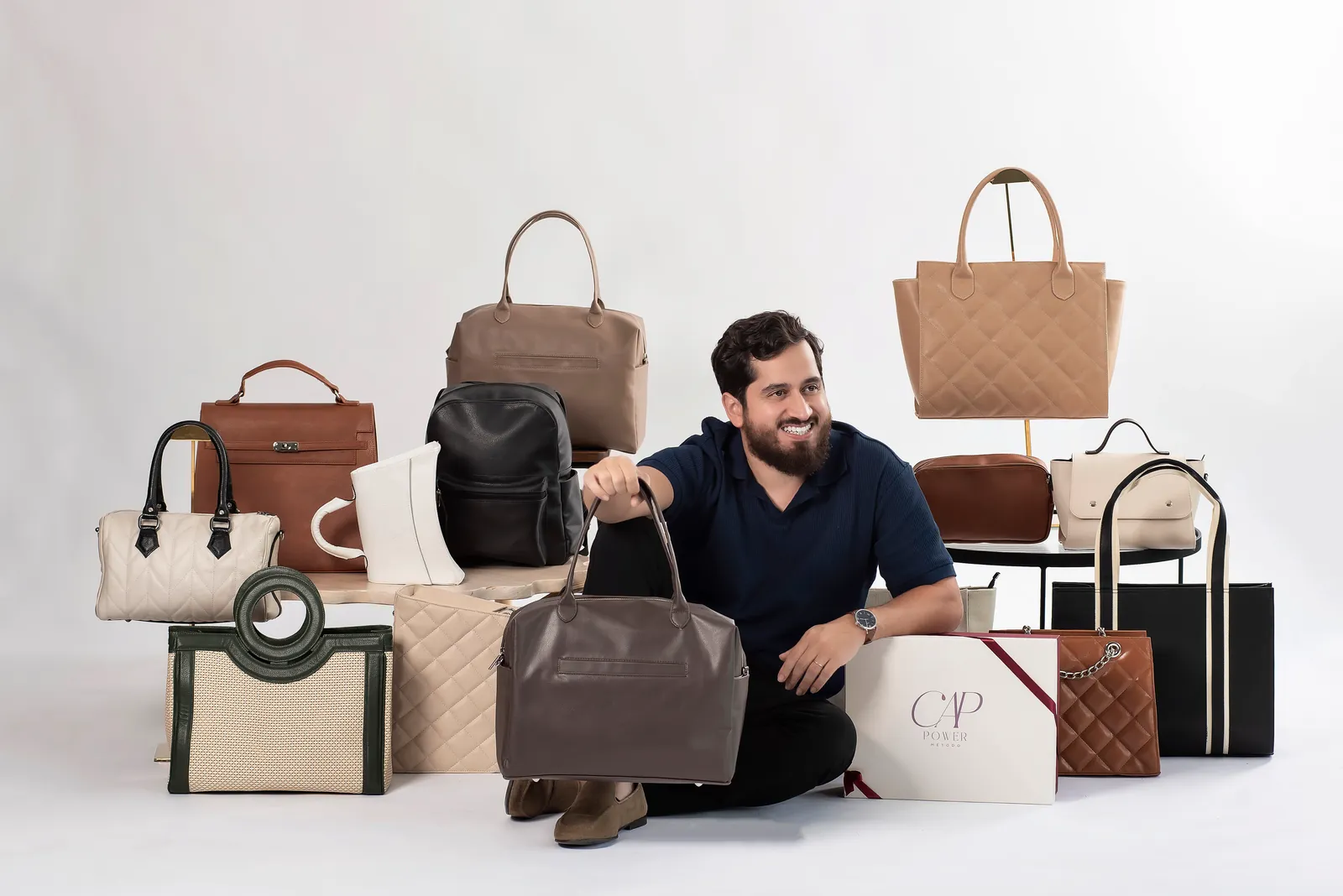 Professor Bruno sentado no chão entre várias Bags da Comunidade Artesã Power, segurando uma delas